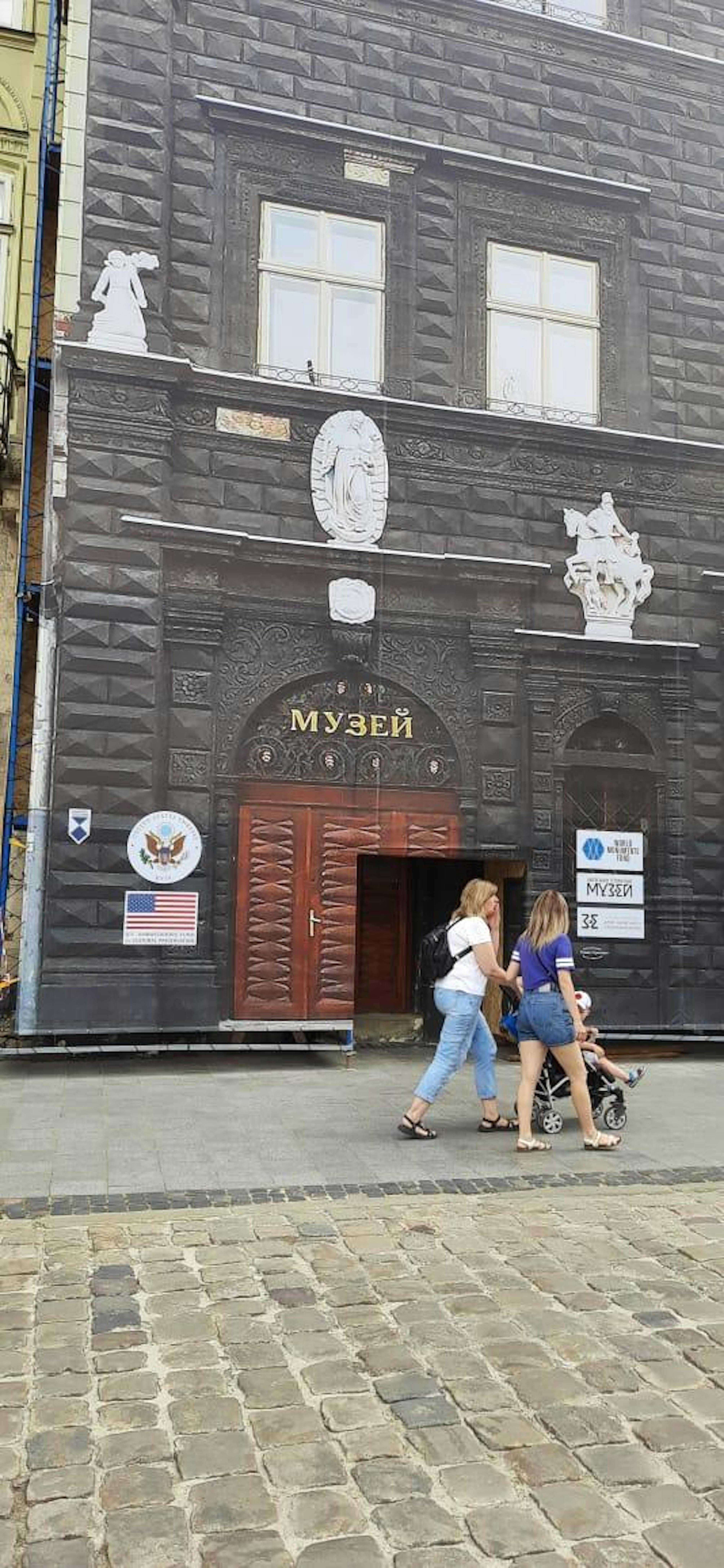 Two women walking past a building whose front is covered by a tarp