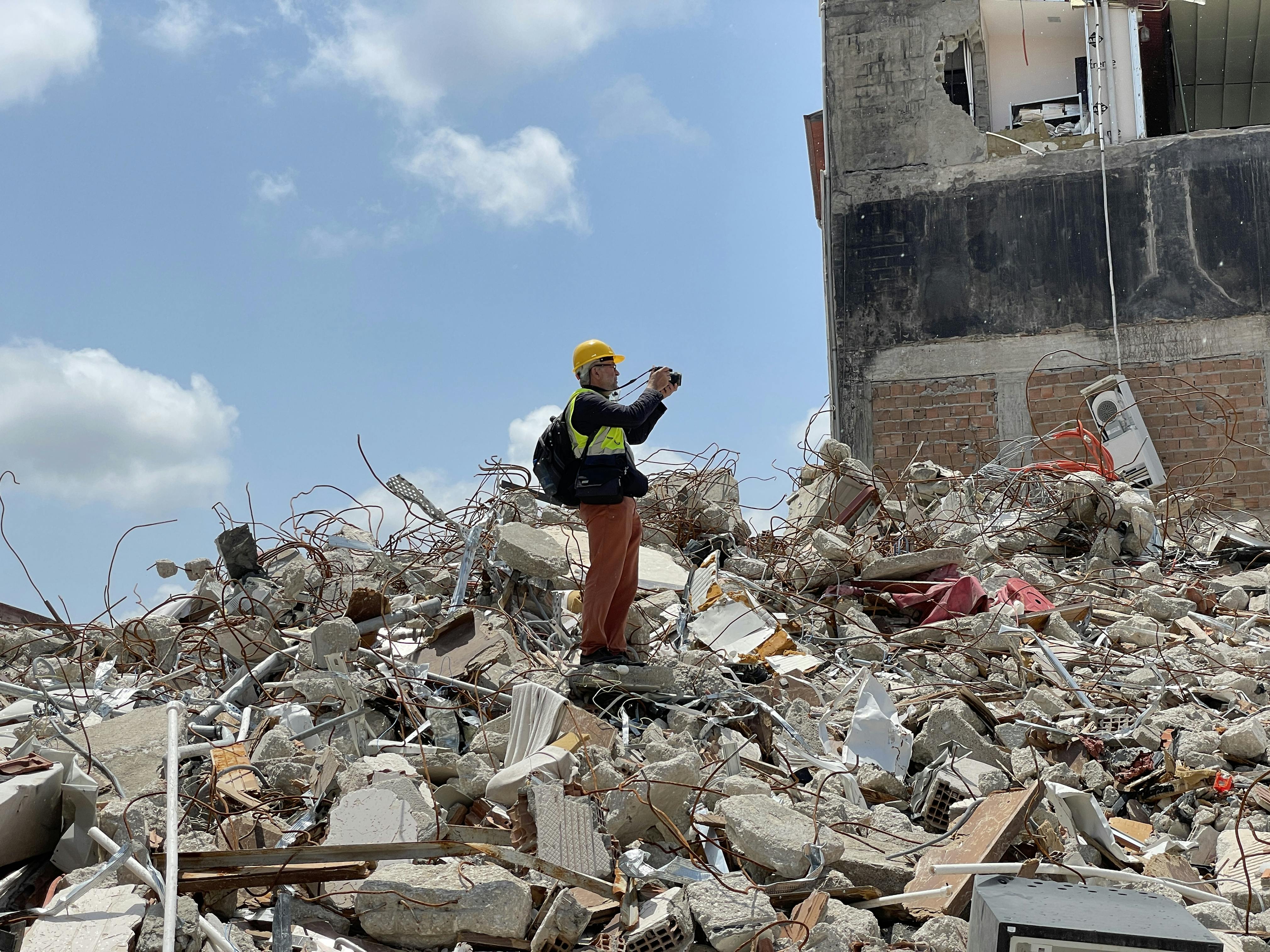 Man in safety gear standing on huge hill of rubble, looking off to the side